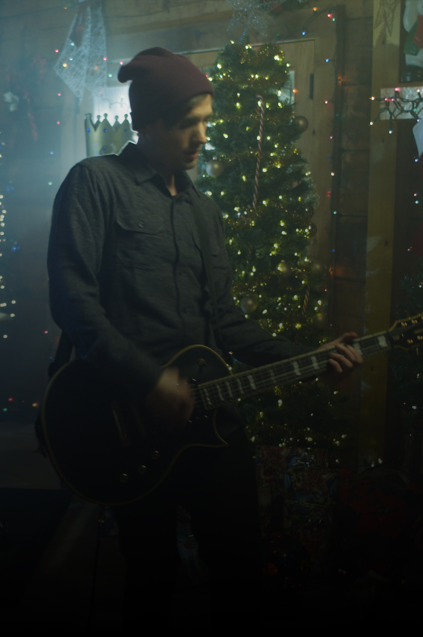 Daniel Deputy of Winona Avenue playing guitar in a cabin decorated for Christmas during the December Night music video shoot.