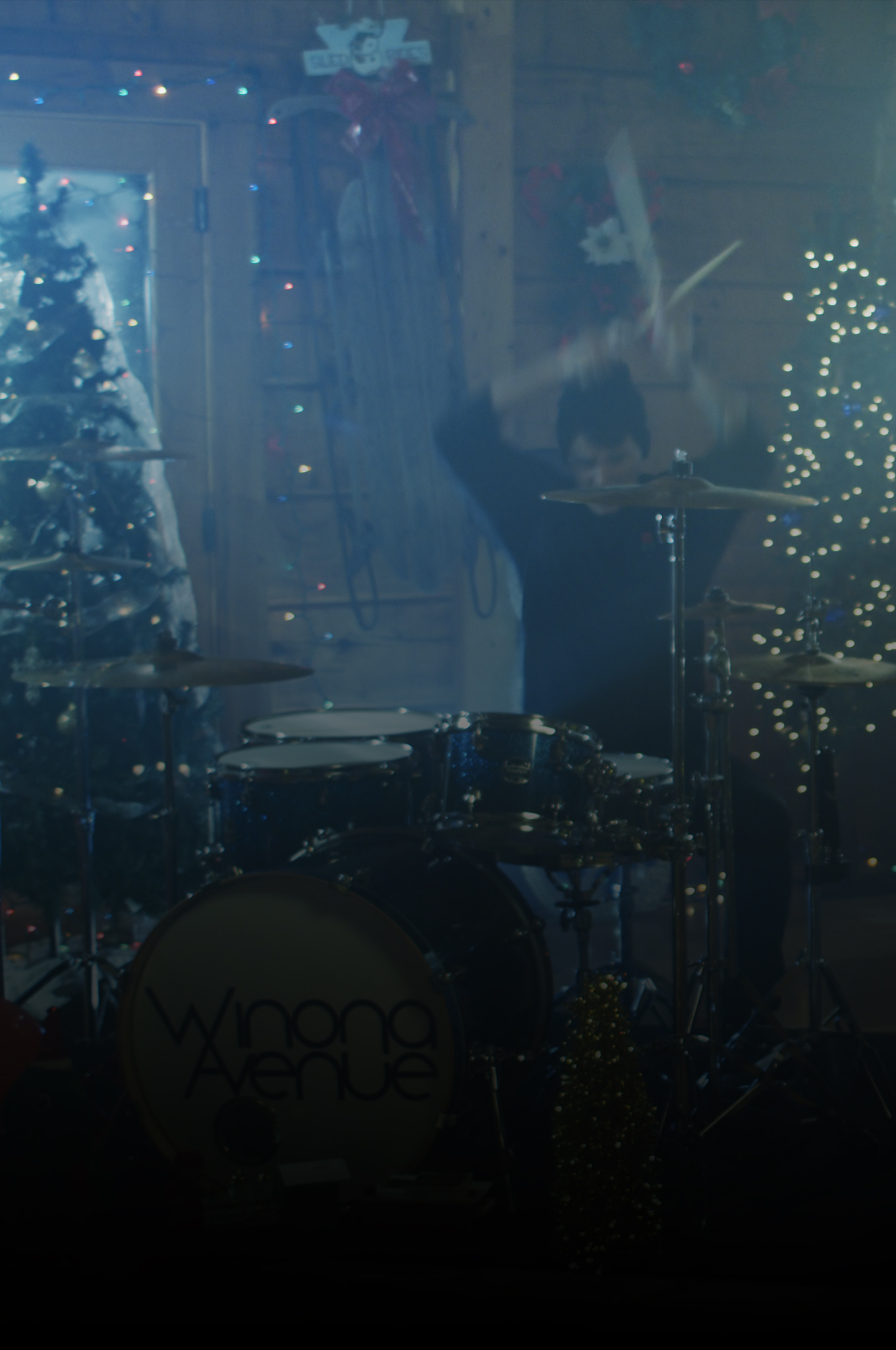 David Deputy of Winona Avenue playing drums in a cabin decorated for Christmas during the December Night music video shoot.
